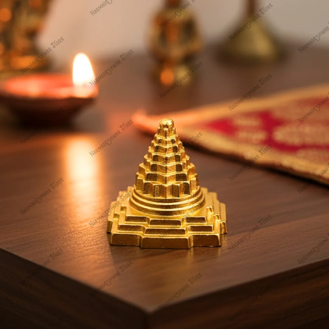 Gold-colored pyramid-shaped Brass Shri Yantra on a wooden surface with a lit candle in the background.