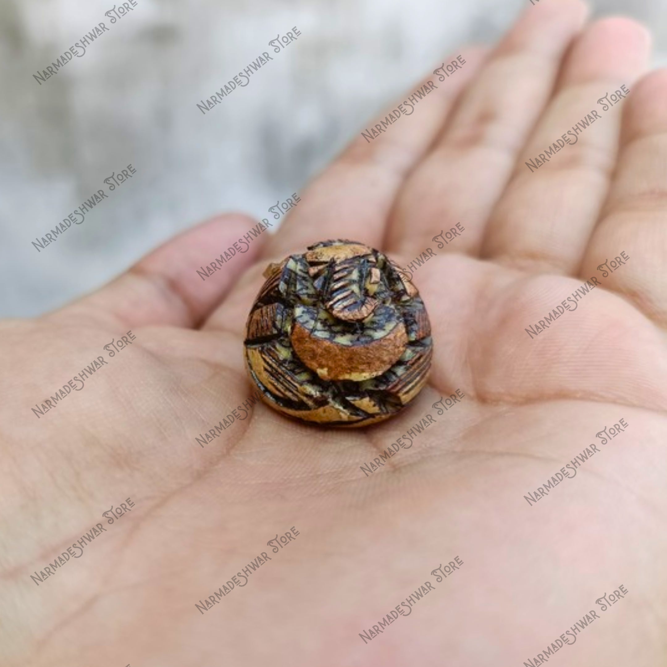 Small, intricately patterned Supari  Ganesh held in a hand with a blurred background